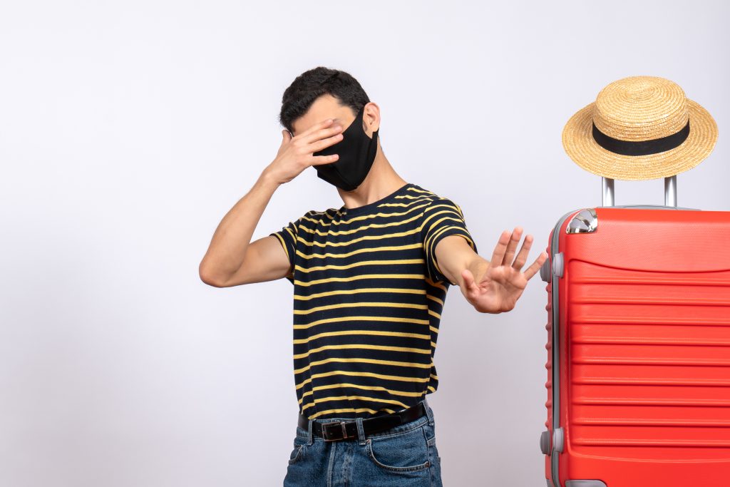 front-view-young-tourist-with-black-mask-standing-near-red-suitcase-closing-his-eyes-with-hand-1024x683.jpg